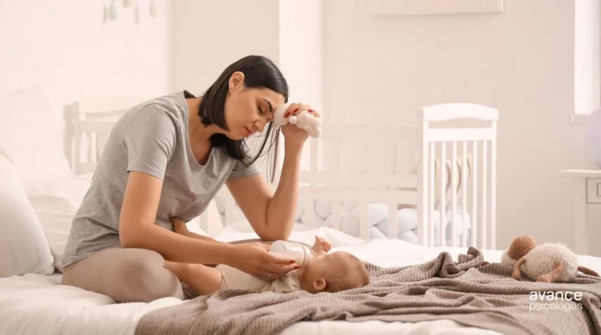 Madre exhausta alimentando a su bebé en la cama mientras muestra signos de fatiga emocional