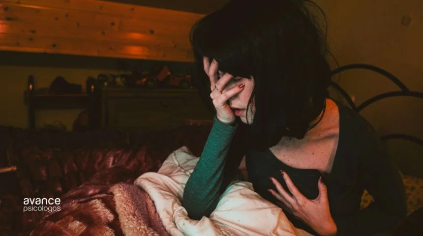 Mujer sentada en la cama con expresión de angustia, llevándose la mano al pecho durante un episodio de ansiedad nocturna