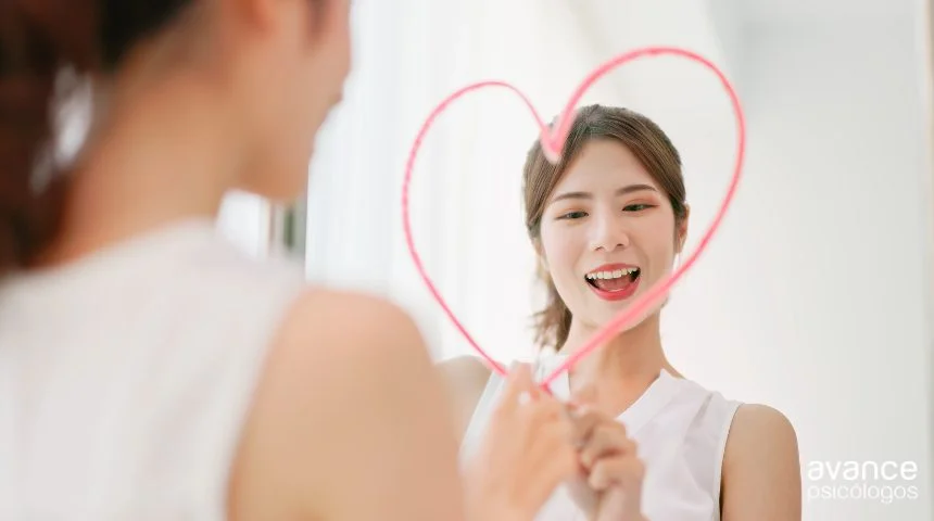 Mujer dibujando un corazón en el espejo con una sonrisa, símbolo visual de autoestima positiva, autoaceptación y cuidado personal.