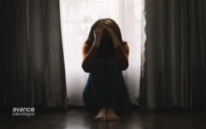 Mujer sentada en el suelo con signos de depresión en un entorno oscuro