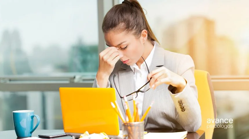 Mujer con dolor de cabeza por estrés laboral frente al portátil